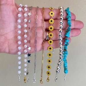 May include: Six different types of chain necklaces with various charms. The chains are silver, gold, and white pearl. The charms include stars, sunflowers, and turquoise stones.
