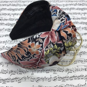 May include: A knotted headband with a black base and a floral patterned top. The floral pattern includes shades of pink, orange, blue, and yellow on a dark background. The brand name "CUCITORINO" is visible on a tag.