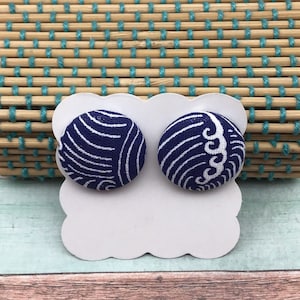 Peut inclure: Une paire de boucles d'oreilles en tissu bleu et blanc avec un motif de vagues. Les boucles d'oreilles sont présentées sur une carte blanche aux bords festonnés.