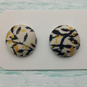 May include: A pair of round stud earrings with a white background and a black and gold floral pattern.