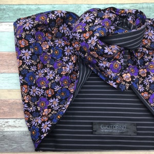 Pode incluir: Um lenço reversível com estampa floral de um lado e listras pretas e brancas do outro. O lenço é feito de um tecido macio e leve e tem uma pequena etiqueta com o texto "Cucitorino - Seja você mesmo, ame a si mesmo."