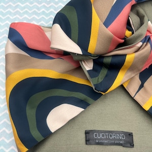 Può includere: Un foulard di seta con motivo verde, blu, giallo e rosa con un'etichetta nera che recita "Cucitorino - Be yourself, love yourself."