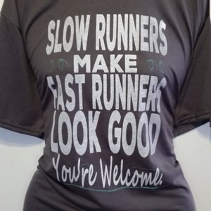 May include: A dark gray t-shirt with a white graphic that reads "Slow Runners Make Fast Runners Look Good You're Welcome."