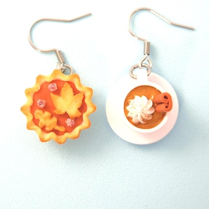 May include: A pair of mismatched dangle earrings featuring a miniature orange pumpkin pie charm with leaf decorations and a miniature white coffee cup charm filled with brown liquid, white whipped cream, and a brown cinnamon stick.
