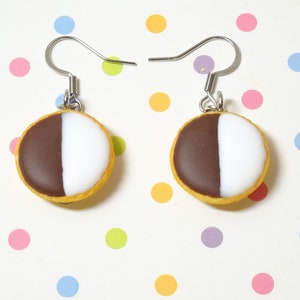 May include: A pair of black and white cookie earrings. The cookies are made of polymer clay and have a realistic look. The earrings are attached to silver hooks.