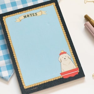 May include: A blue notepad with a rope border and a white dog wearing a red hat in a red boat. The notepad has the word "NOTES" written on it.