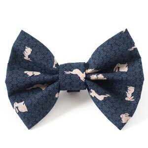 Puede incluir: Una pajarita azul marino con un estampado repetido de conejos blancos y un diseño de ondas. Un accesorio clásico, adecuado para ocasiones formales o informales.
