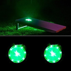 May include: Two green LED light-up cornhole bags with a star design. The bags are illuminated with a bright green light.