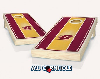 May include: Two wooden cornhole boards with a maroon and gold striped design. The boards feature a white circle in the center and a stylized letter "C" in the middle of the board. The boards are set up for a game of cornhole.