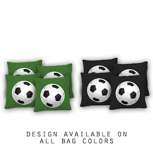 May include: Six bean bags with a soccer ball design. Three bean bags are green and three are black. The text "DESIGN AVAILABLE ON ALL BAG COLORS" is below the bean bags.
