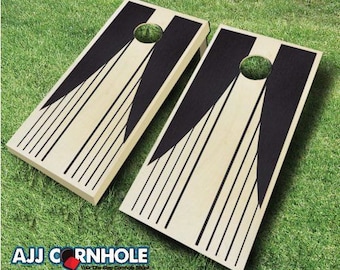 May include: Two wooden cornhole boards with a black and white geometric design. The boards have a black stripe down the center and black lines radiating out from the center.
