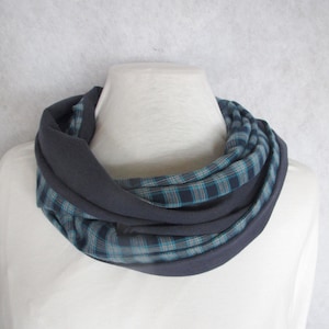 May include: A dark grey infinity scarf with a blue and teal plaid pattern. The scarf is displayed on a mannequin, highlighting its design and texture. This accessory is suitable for cooler weather.