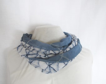 May include: A blue and white patterned scarf made of soft fabric. The scarf is folded and displayed on a white mannequin.