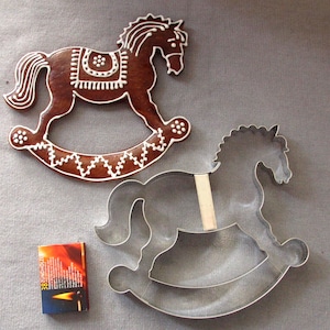 May include: A gingerbread rocking horse cookie decorated with white icing and a metal rocking horse cookie cutter.