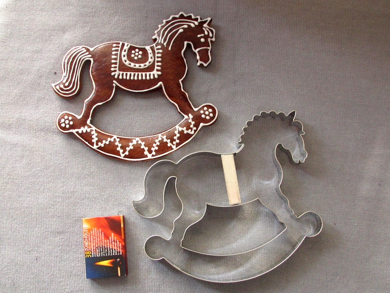 May include: A gingerbread rocking horse cookie decorated with white icing and a metal rocking horse cookie cutter.