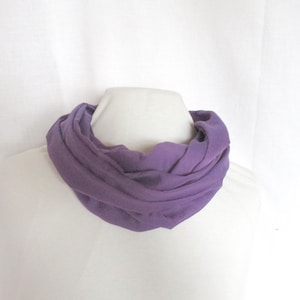 Könnte beinhalten: Ein weicher, lilafarbener Infinity-Schal aus leichtem Stoff. Der Schal ist zu einer Schleife gefaltet und über eine weiße Oberfläche gelegt.