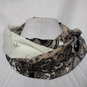Peut inclure: Une écharpe infinie à motif paisley brun et blanc avec une doublure en tissu crème. La doublure est ornée d'un motif brodé doré.