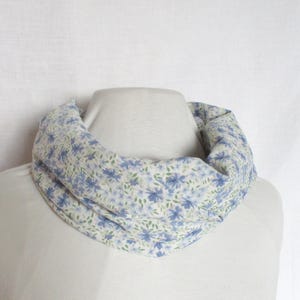 May include: A blue and green floral print infinity scarf on a cream background. The scarf is displayed on a mannequin, highlighting its circular design. The fabric looks soft and lightweight, ideal for spring or summer wear. The scarf is approximately 150 cm in circumference.