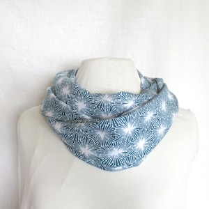 以下が含まれることがあります： 白いマネキンに飾られた、青と白の模様のインフィニティスカーフ。スカーフは、青い背景に白い星型のデザインが繰り返されています。生地は柔らかく、軽量に見えます。