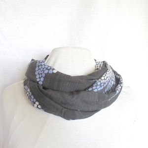 Könnte beinhalten: Dunkelgrauer Loop-Schal mit einem Muster aus kleinen, hellblauen und weißen Punkten. Der Schal ist um einen weißen Schaufensterkopf drapiert, um sein Design und seine Textur zu zeigen. Der Schal scheint aus einem weichen, leichten Stoff zu sein.