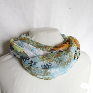Op de afbeelding: Een blauwe, groene, oranje en witte gestreepte sjaal met een paisley-patroon.