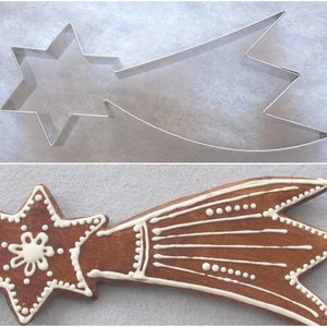 Könnte beinhalten: Ein Ausstecher in Form eines Sterns aus Edelstahl und ein dekorierter Lebkuchen in Form eines Sterns. Der Keks ist braun mit weißen Zuckergussdetails, einschließlich eines Sterns und Linien.