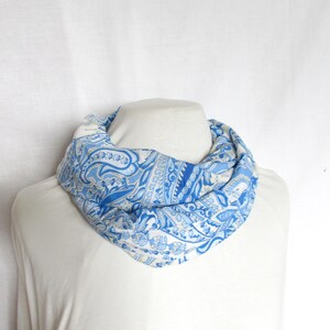 Könnte beinhalten: Ein weißer und blauer Paisley-Muster-Infinity-Schal. Der Schal ist aus einem weichen, leichten Stoff gefertigt und perfekt, um jedem Outfit einen Hauch von Stil zu verleihen.