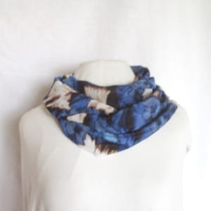 Op de afbeelding: Een blauw-witte infinity sjaal met patroon. De sjaal is om een witte mannequin gewikkeld. Het patroon bevat tinten blauw, wit en bruin. De sjaal is gemaakt van een zacht, lichtgewicht materiaal.