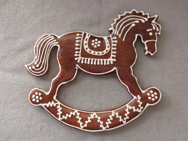 May include: A brown gingerbread rocking horse decorated with white icing. The horse has a saddle and a mane, and the rocking base is decorated with a white zig-zag pattern.