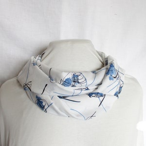 Könnte beinhalten: Weißer Schal mit abstraktem Design in Blau und Schwarz. Der Schal ist gefaltet und auf einer weißen Schaufensterpuppe ausgestellt.