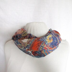 Könnte beinhalten: Ein farbenfroher Schlauchschal mit Paisley-Muster. Der Schal zeigt eine Mischung aus Orange, Blau und Weiß. Er ist um eine weiße Schaufensterpuppe gelegt, um sein Design und seine Form zu präsentieren.