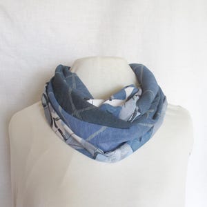 Op de afbeelding: Een blauw-witte infinity sjaal op een mannequin. De sjaal heeft een ruitpatroon in tinten blauw, grijs en wit. De stof lijkt zacht en lichtgewicht, geschikt voor koeler weer. De sjaal is om de nek van de mannequin gewikkeld.