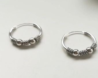 May include: A pair of silver hoop earrings with three small silver beads on each hoop.