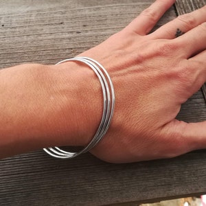 Peut inclure: Un ensemble de trois bracelets en argent empilés sur le poignet d'une personne.