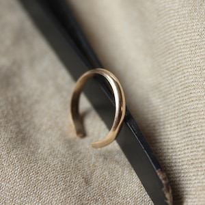 Può includere: Un anello dorato con una superficie liscia e arrotondata. L'anello è tenuto da una pinzetta nera.
