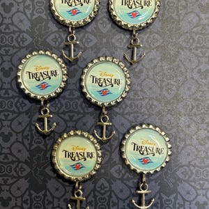 May include: Six gold bottle cap charms with a blue and white design that says "Disney Treasure" with a red Mickey Mouse head and a gold anchor charm hanging from each.