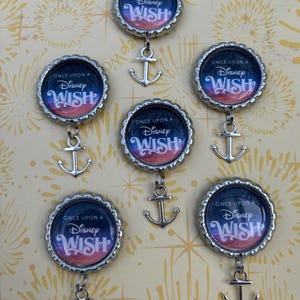 May include: A collection of seven bottle cap pendants. Each pendant features the text "ONCE UPON A Disney WISH" in white on a dark blue and pink background. A silver anchor charm hangs below each cap.