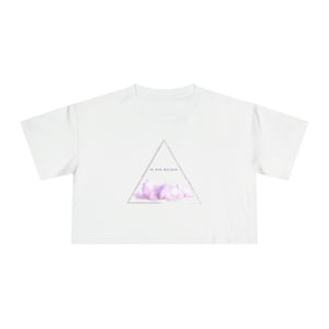 Puede incluir: Una camiseta blanca recortada con un gráfico triangular que presenta una nube de acuarela rosa y púrpura. El texto "IN DEN WOLKEN" está dentro del triángulo.