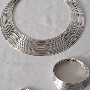 Könnte beinhalten: Ein Set aus silbernem Schmuck, bestehend aus einer Halskette, zwei Paar Ohrringen, einem Armband und einem Ring. Alle Stücke sind aus dünnem, geschichtetem Metall gefertigt.