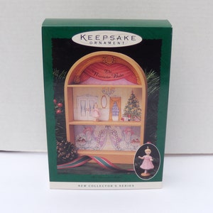 May include: A green box featuring a Christmas ornament. The ornament depicts a miniature stage with a ballerina, a Christmas tree, and the words "The Nutcracker Ballet." The box also includes a miniature ballerina ornament.