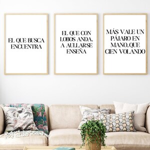 May include: Three framed prints with Spanish text on a white wall. The text on the prints reads: "El que busca encuentra", "El que con lobos anda, a aullarse enseña", and "Más vale un pájaro en mano, que cien volando".