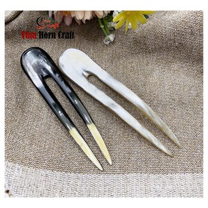 Puede incluir: Dos horquillas para el cabello hechas de cuerno. Una es negra y la otra blanquecina. Ambas tienen un dise&ntilde;o de dos puntas con un acabado liso y pulido. Las puntas de la horquilla negra son de color amarillo claro. Miden unos 15 cm.