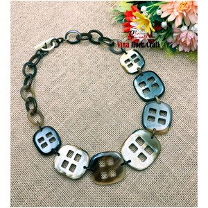 May include: A brown and black horn necklace with a chain made of black and white plastic rings. The necklace features a series of square-shaped pendants with a cut-out design. The text "Vina Horn Craft" is visible in the image.