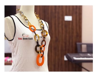 May include: A long necklace made of brown, black, and orange horn circles. The necklace is on a white mannequin.