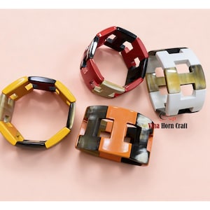 May include: Four colorful geometric bracelets. One is yellow and black, another is red and black, a third is white and tan, and the last is orange and brown. The bracelets are made of a hard material and have a repeating geometric pattern.