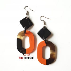Peut inclure: Une paire de boucles d'oreilles en corne orange et noire avec un pendentif en forme de diamant. Les boucles d'oreilles sont en corne et ont un crochet argenté.