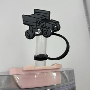 以下が含まれることがあります： ステンレス製のタンブラー用のピンクと透明なプラスチック製の蓋に、白黒のレースカーのイラストが描かれています。