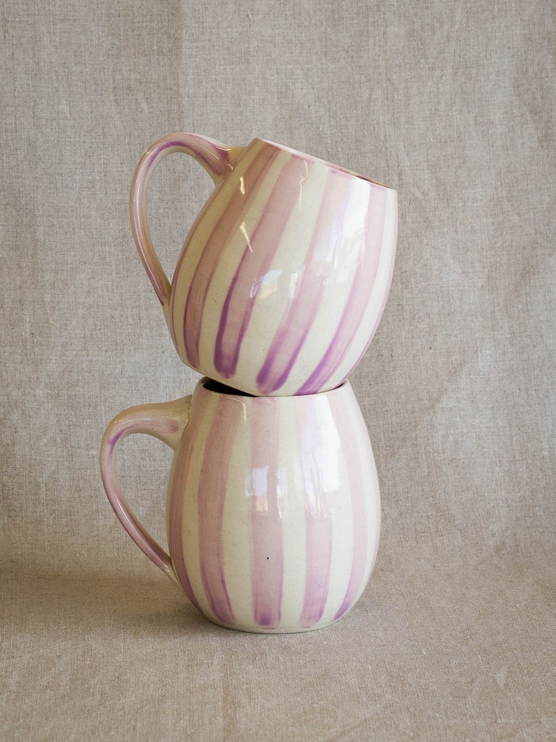 A stack of handmade mugs with a glossy glaze and hand painted purple stripes