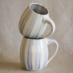 A stack of two handmade ceramic mugs with hand painted vertical stripes in a light periwinkle color