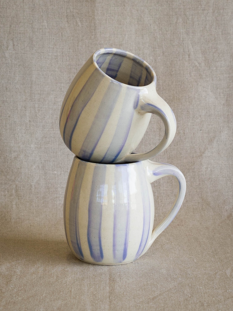 A stack of two handmade ceramic mugs with hand painted vertical stripes in a light periwinkle color